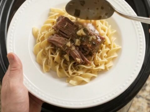 Fork-tender beef brisket with shallots and carrots in a slow cooker, topped with melted garlic butter