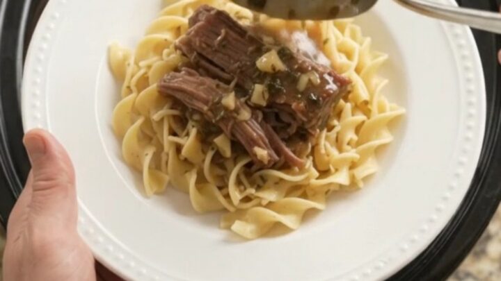 Fork-tender beef brisket with shallots and carrots in a slow cooker, topped with melted garlic butter