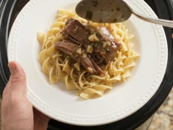 Fork-tender beef brisket with shallots and carrots in a slow cooker, topped with melted garlic butter