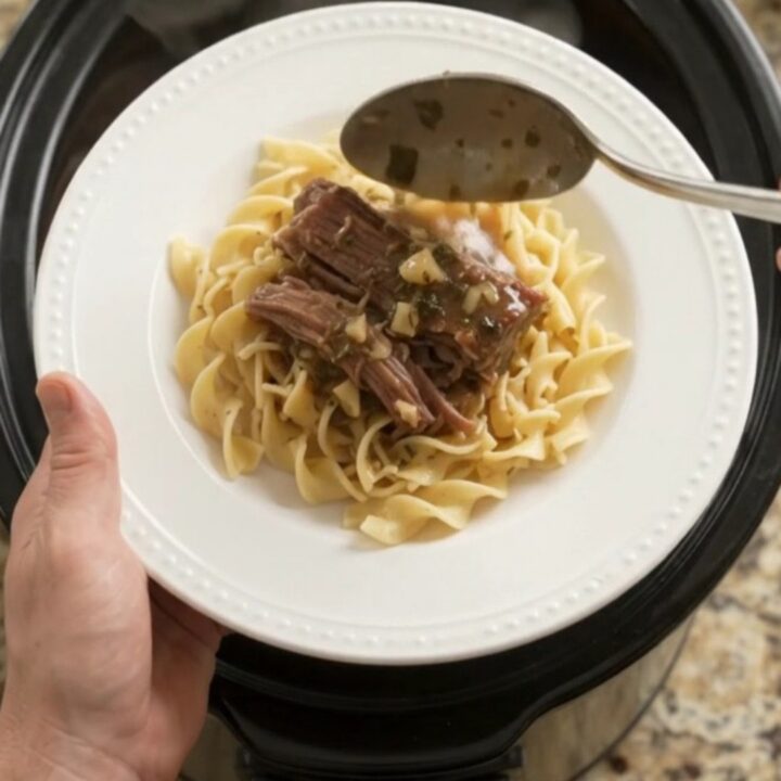 Fork-tender beef brisket with shallots and carrots in a slow cooker, topped with melted garlic butter