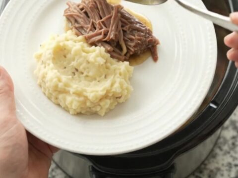 Shredded beef brisket with potatoes and carrots in a slow cooker, coated in buttery jus.
