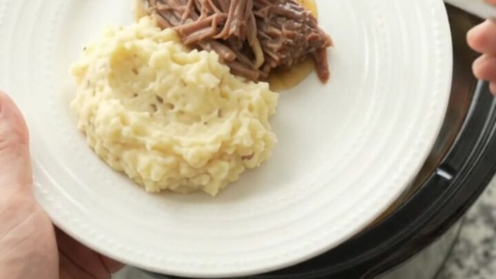 Shredded beef brisket with potatoes and carrots in a slow cooker, coated in buttery jus.