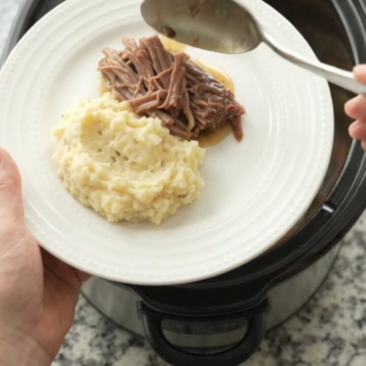 Shredded beef brisket with potatoes and carrots in a slow cooker, coated in buttery jus.