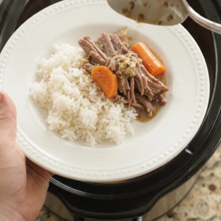 Slow-cooker brisket with potatoes and carrots in creamy Dijon gravy, in a black ceramic pot