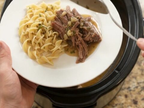 Fork-tender shredded beef brisket with potatoes and carrots in a slow cooker, topped with garlic butter gravy.