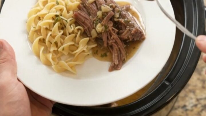 Fork-tender shredded beef brisket with potatoes and carrots in a slow cooker, topped with garlic butter gravy.