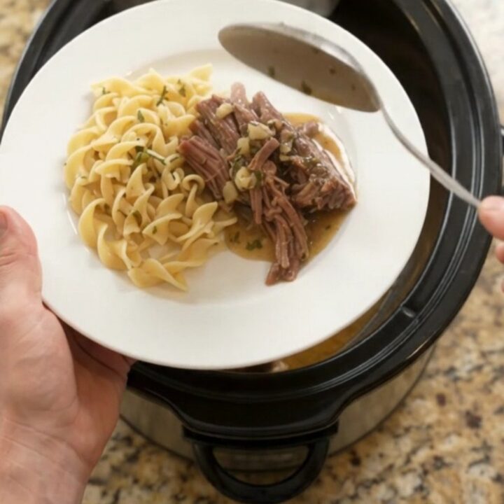 Fork-tender shredded beef brisket with potatoes and carrots in a slow cooker, topped with garlic butter gravy.