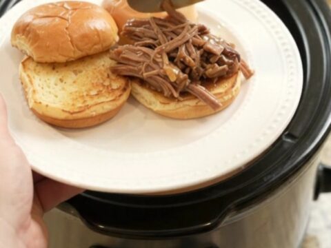 Slow-cooked beef brisket with portobello mushrooms in rich brown gravy, served in a black ceramic slow cooker.