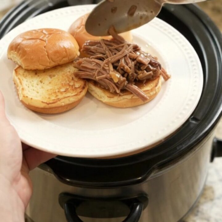 Slow-cooked beef brisket with portobello mushrooms in rich brown gravy, served in a black ceramic slow cooker.