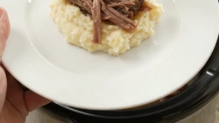 Shredded beef brisket with peppers and onions in a slow cooker, golden juices bubbling
