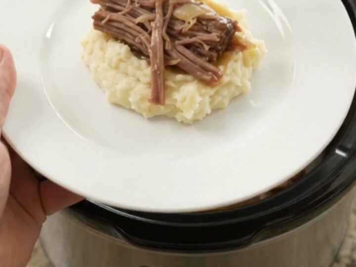 Shredded beef brisket with peppers and onions in a slow cooker, golden juices bubbling