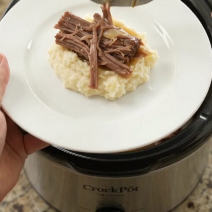 Shredded beef brisket with peppers and onions in a slow cooker, golden juices bubbling