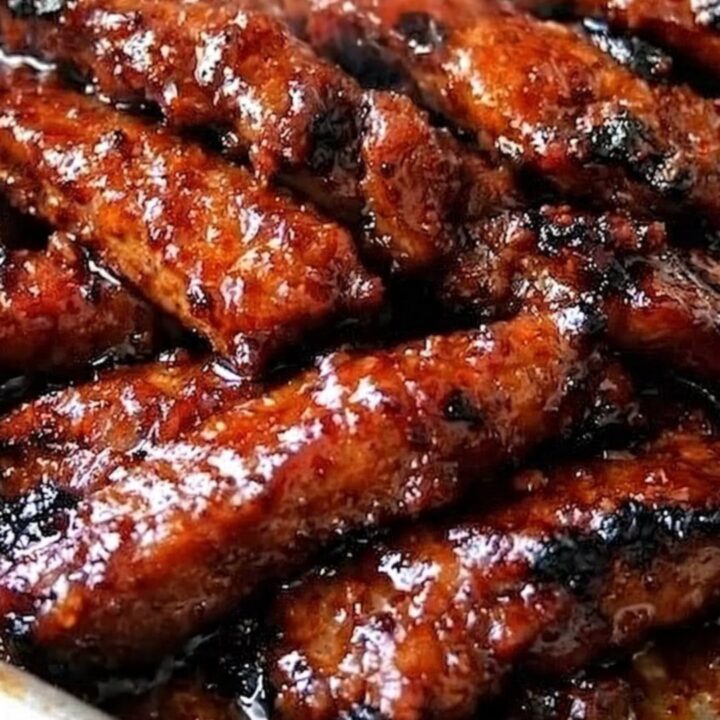 A rustic metal tray piled high with deeply caramelized, glossy honey-garlic glazed pork ribs with visible steam.