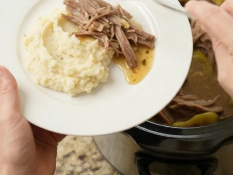 Slow cooker pork shoulder with pepperoncini and butter in a black ceramic crock