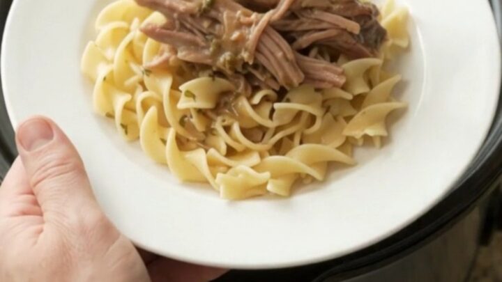 Shredded pepperoncini ranch garlic butter pork in a slow cooker, with buttered egg noodles