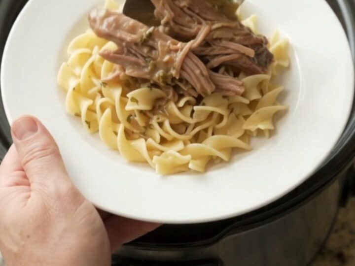 Shredded pepperoncini ranch garlic butter pork in a slow cooker, with buttered egg noodles