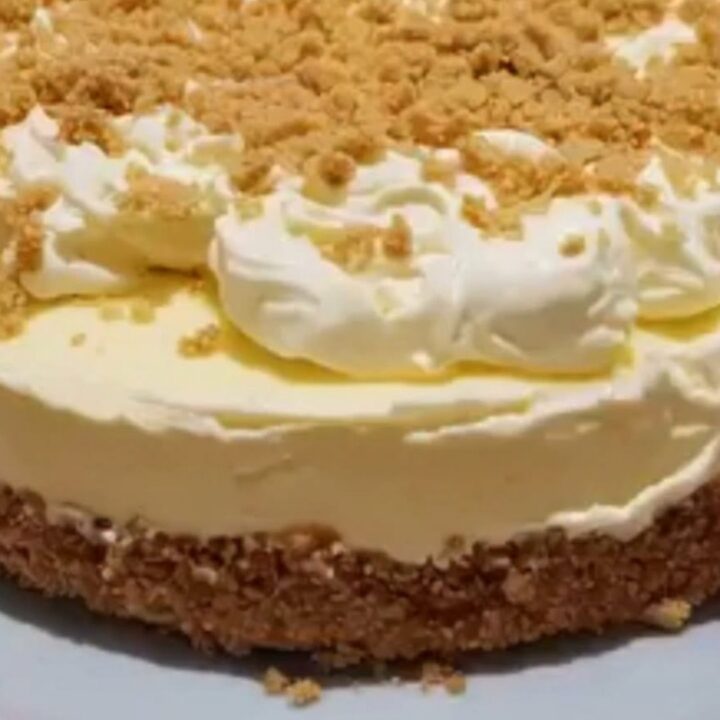 Whole chilled condensed milk cheesecake topped with piped whipped cream rosettes and crushed biscuit crumbs.