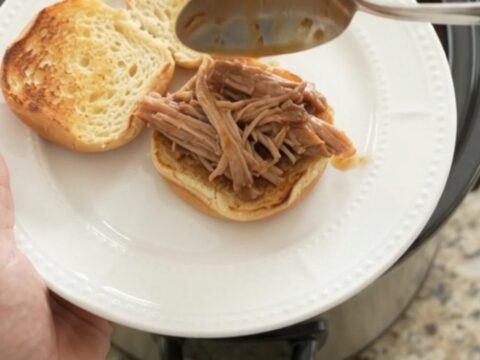 Slow cooker pork shoulder in rich brown gravy, garnished with fresh herbs, on a wooden board