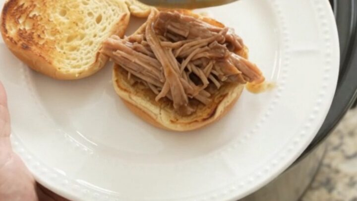 Slow cooker pork shoulder in rich brown gravy, garnished with fresh herbs, on a wooden board