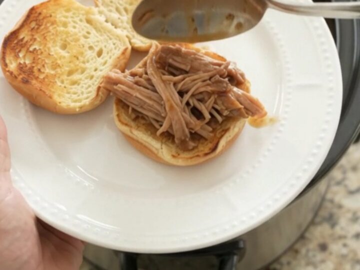 Slow cooker pork shoulder in rich brown gravy, garnished with fresh herbs, on a wooden board