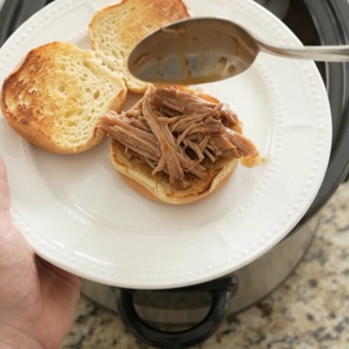 Slow cooker pork shoulder in rich brown gravy, garnished with fresh herbs, on a wooden board