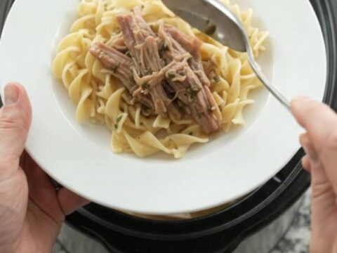 Shredded pork shoulder in a slow cooker with pearl onions and dark stout gravy, topped with melted butter.