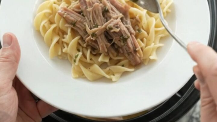 Shredded pork shoulder in a slow cooker with pearl onions and dark stout gravy, topped with melted butter.