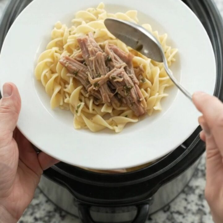 Shredded pork shoulder in a slow cooker with pearl onions and dark stout gravy, topped with melted butter.