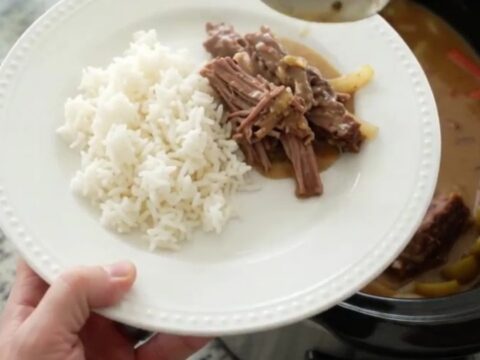Slow-cooker pork shoulder with pearl onions and Guinness gravy in a black crockpot, garnished with fresh thyme.