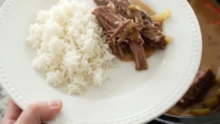 Slow-cooker pork shoulder with pearl onions and Guinness gravy in a black crockpot, garnished with fresh thyme.