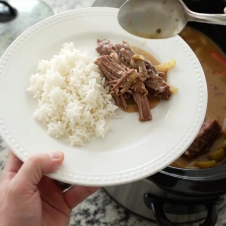 Slow-cooker pork shoulder with pearl onions and Guinness gravy in a black crockpot, garnished with fresh thyme.