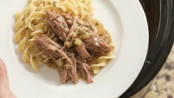 Slow-cooker pork shoulder with shallots and carrots in a black ceramic pot, topped with garlic butter