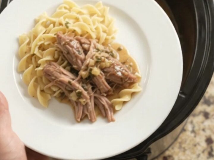 Slow-cooker pork shoulder with shallots and carrots in a black ceramic pot, topped with garlic butter