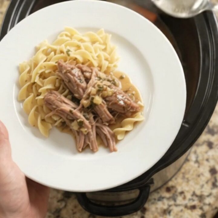 Slow-cooker pork shoulder with shallots and carrots in a black ceramic pot, topped with garlic butter