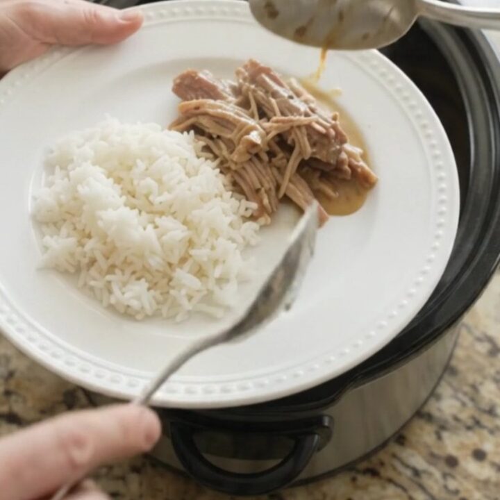 Slow cooker pork shoulder with creamy Dijon sauce, garlic, and fresh herbs in a black crockpot