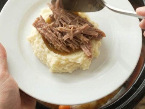 Pulled pork shoulder with carrots and shallots in a slow cooker, topped with melted butter and juices.