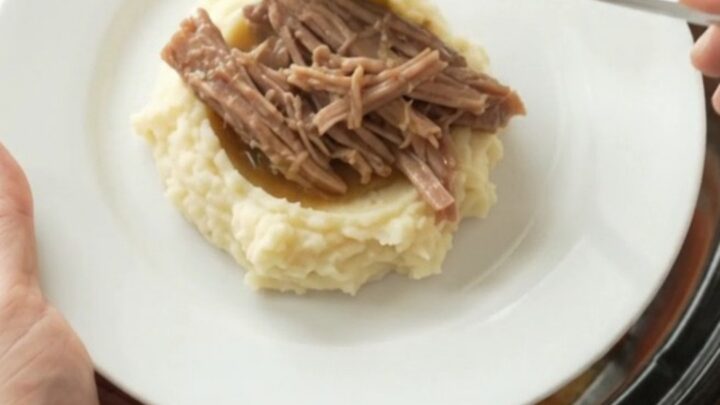 Pulled pork shoulder with carrots and shallots in a slow cooker, topped with melted butter and juices.