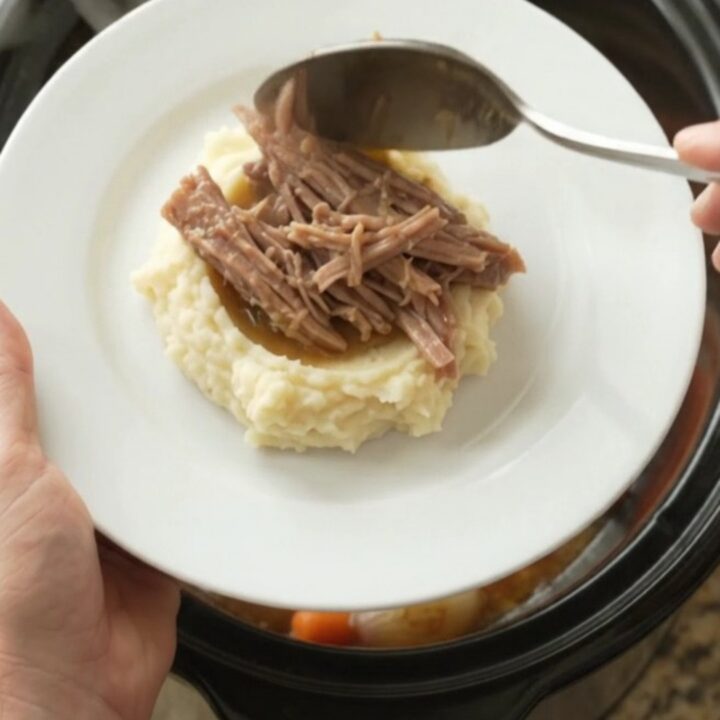 Pulled pork shoulder with carrots and shallots in a slow cooker, topped with melted butter and juices.