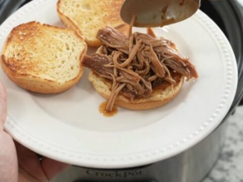 Slow cooker pork shoulder with rosemary and thyme in rich brown gravy, garnished with fresh herbs.