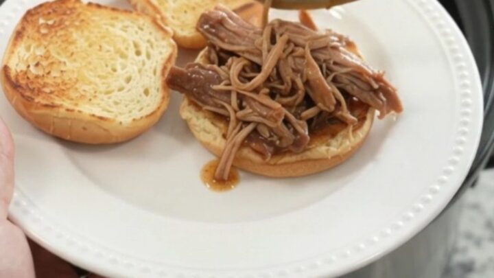 Slow cooker pork shoulder with rosemary and thyme in rich brown gravy, garnished with fresh herbs.