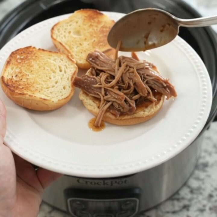 Slow cooker pork shoulder with rosemary and thyme in rich brown gravy, garnished with fresh herbs.