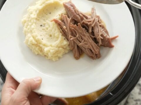 Slow-cooked pork shoulder with baby potatoes and carrots in a black Crockpot, topped with melted butter and fresh herbs