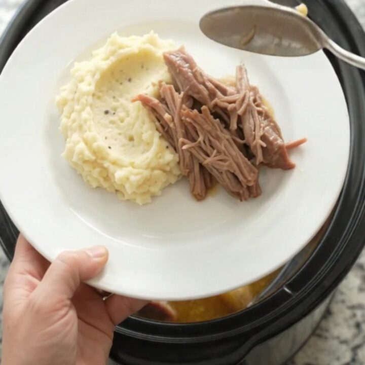 Slow-cooked pork shoulder with baby potatoes and carrots in a black Crockpot, topped with melted butter and fresh herbs