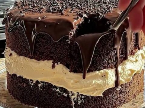 A tall, two-layer chocolate cake with glossy ganache drips and sprinkles on a glass stand.