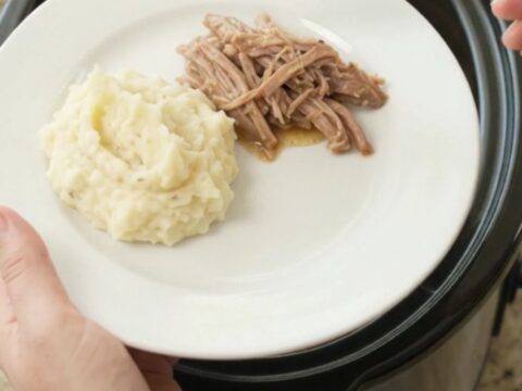 Slow cooker pork shoulder with peppers and onions in a glossy black crock