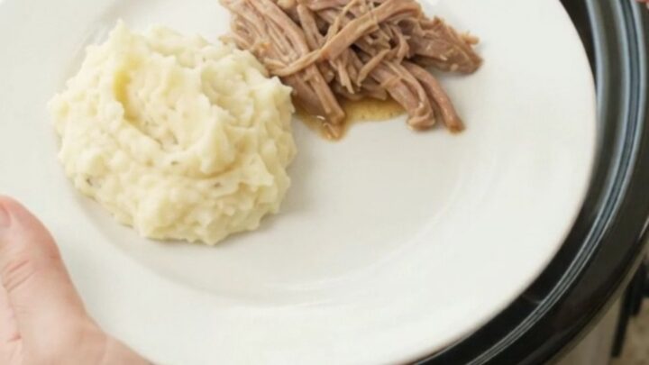 Slow cooker pork shoulder with peppers and onions in a glossy black crock