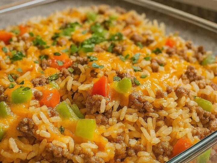 A steaming portion of cheesy ground beef and rice casserole in a glass dish with a melted cheese stretch.