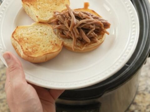 Slow-cooked pork shoulder with sweet peppers in a rich brown gravy, shown in a black Crockpot insert