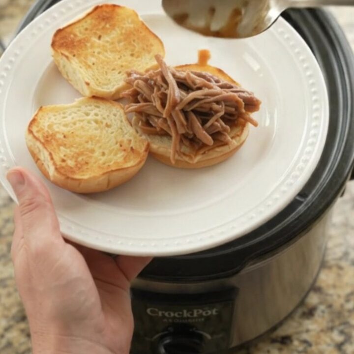 Slow-cooked pork shoulder with sweet peppers in a rich brown gravy, shown in a black Crockpot insert