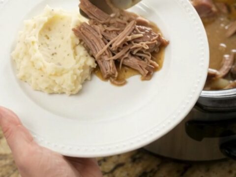 Shredded pork sirloin roast with mushrooms in a slow cooker, topped with butter sauce